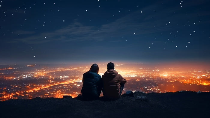 Couple on a hill above a city, looking into the night sky